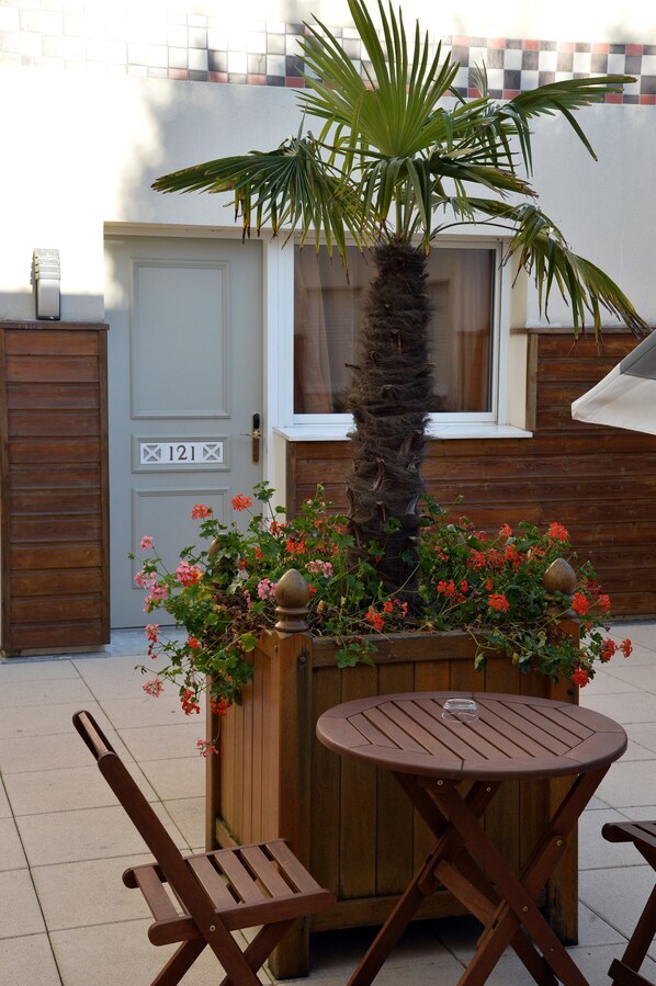 A wooden bench and table set outdoors with a potted plant and flowers.