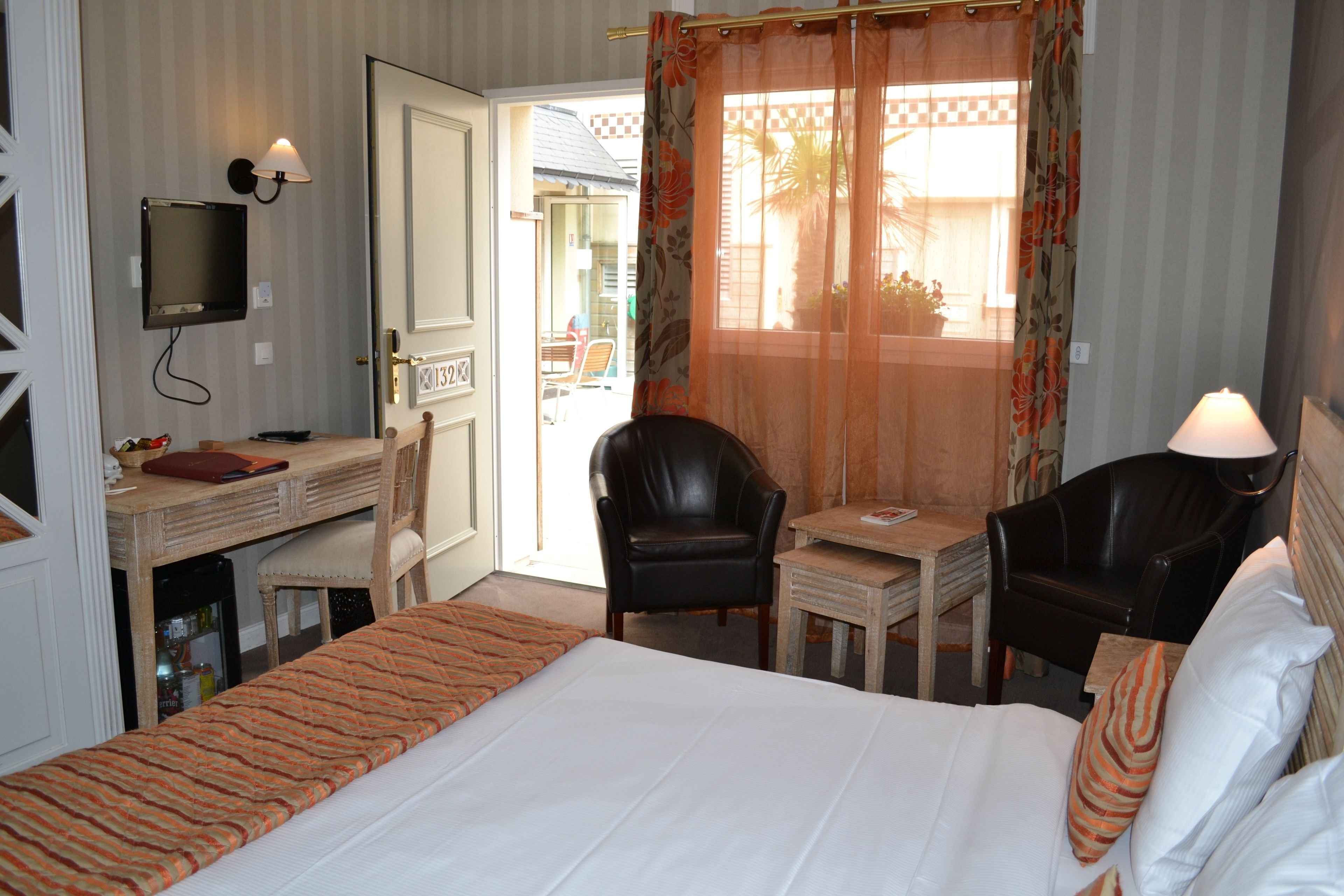 Habitación de hotel con cama, escritorio, dos sillas, televisor y ventana con cortinas.