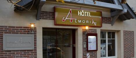 Een hotel genaamd "HOTEL L'AMORIA" met een gevel van baksteen, een glazen ingang en een bord boven de deur.