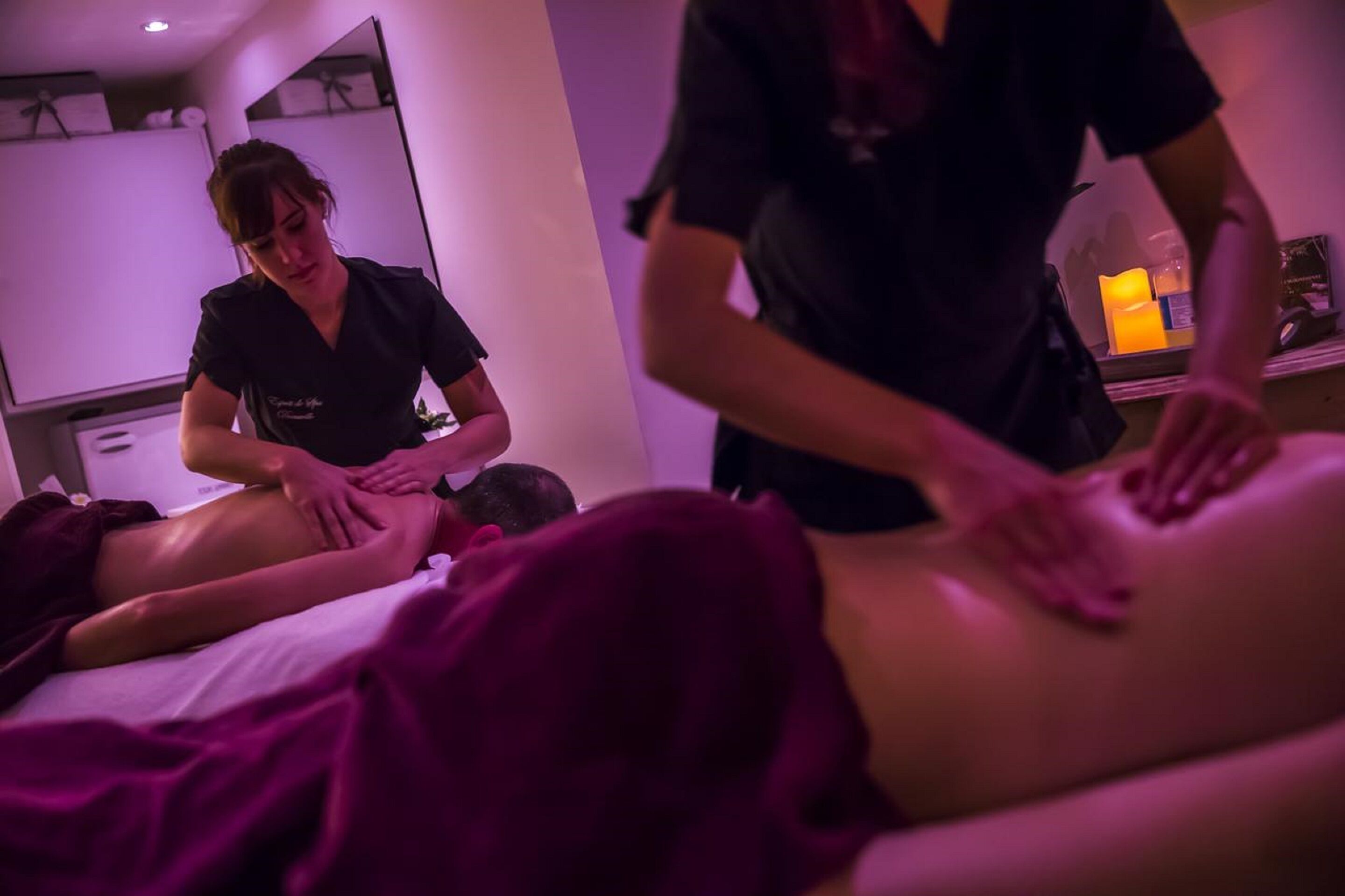 A massage therapy session in a room with a bed, a massage table, and a person receiving a back massage.