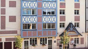 Un edificio de varios pisos con una fachada distintiva que presenta una torre central con techo a punta y una serie de ventanas.