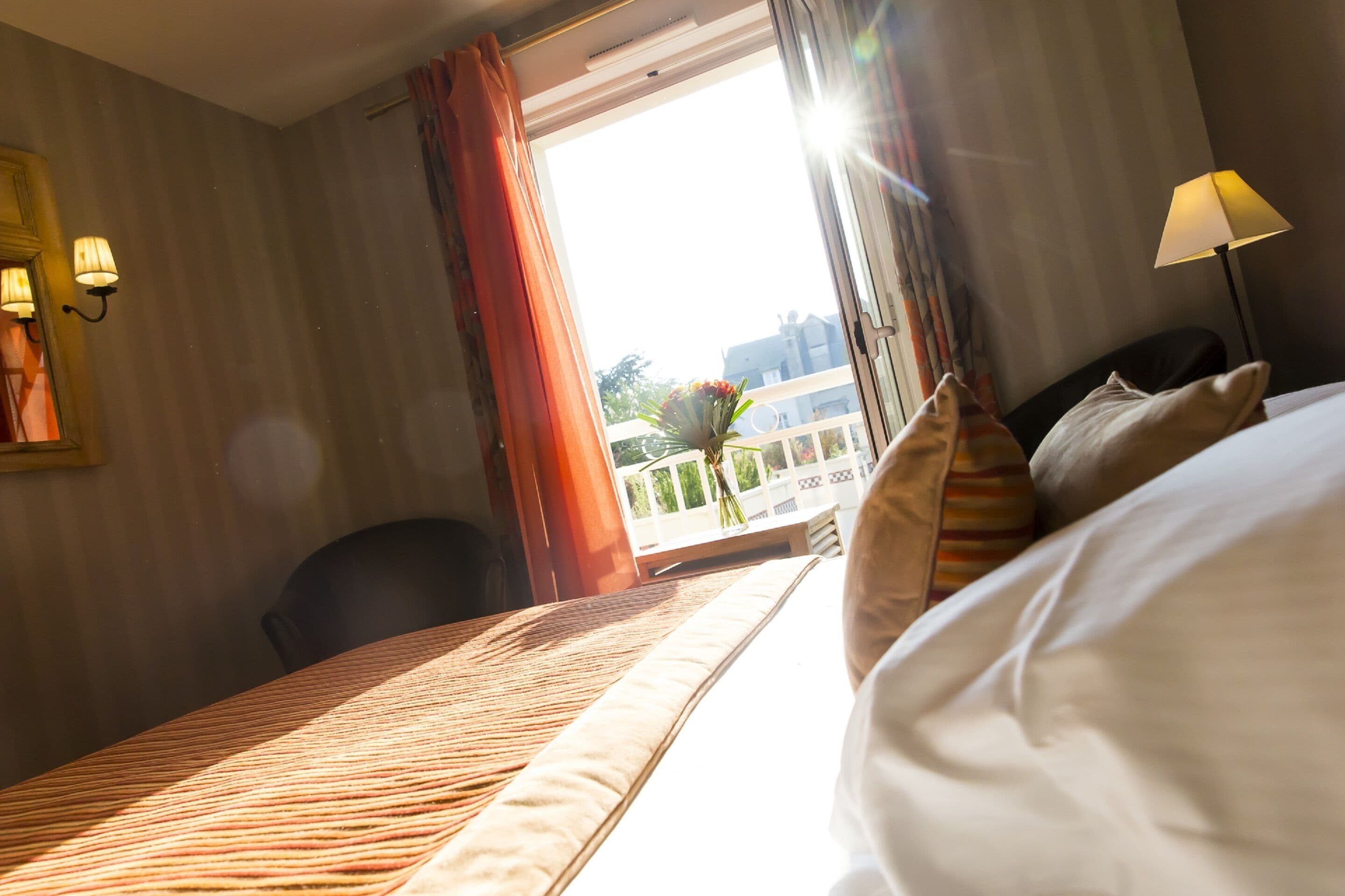 A hotel room with a bed, a chair, a lamp, and a window with curtains.