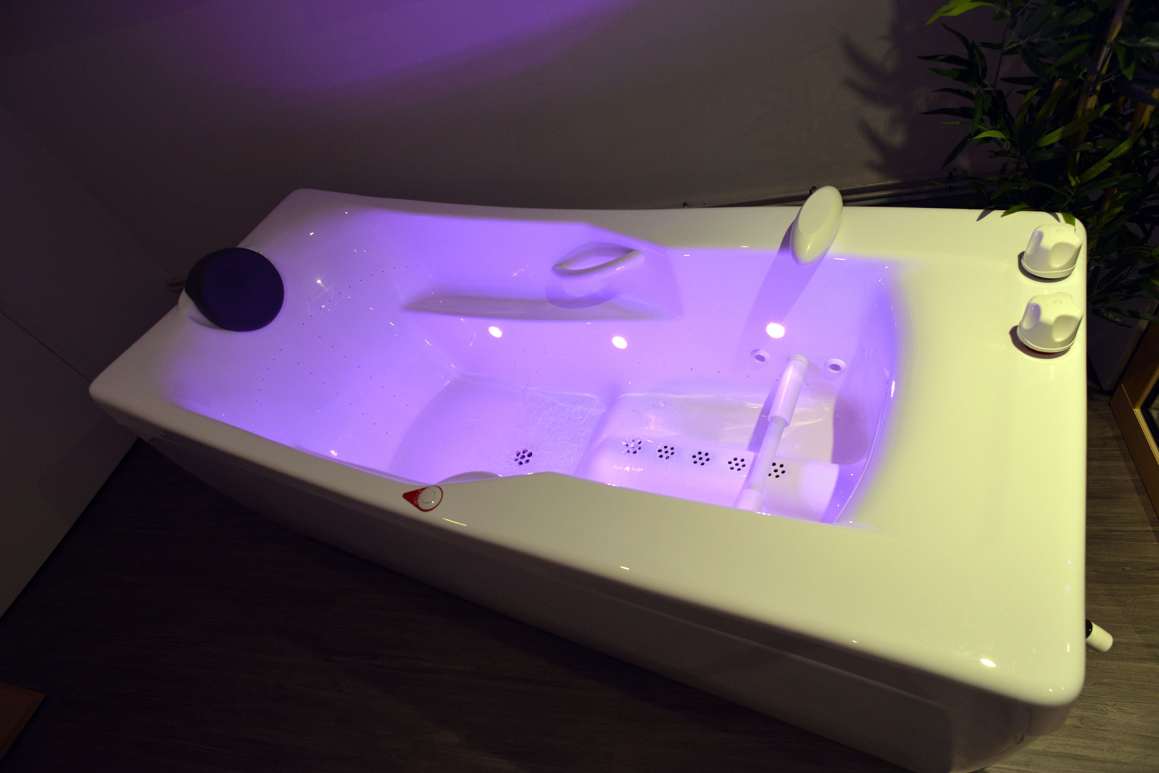Una bañera de hidromasaje blanca con luz morada, un panel de control y dos pequeñas tazas blancas.