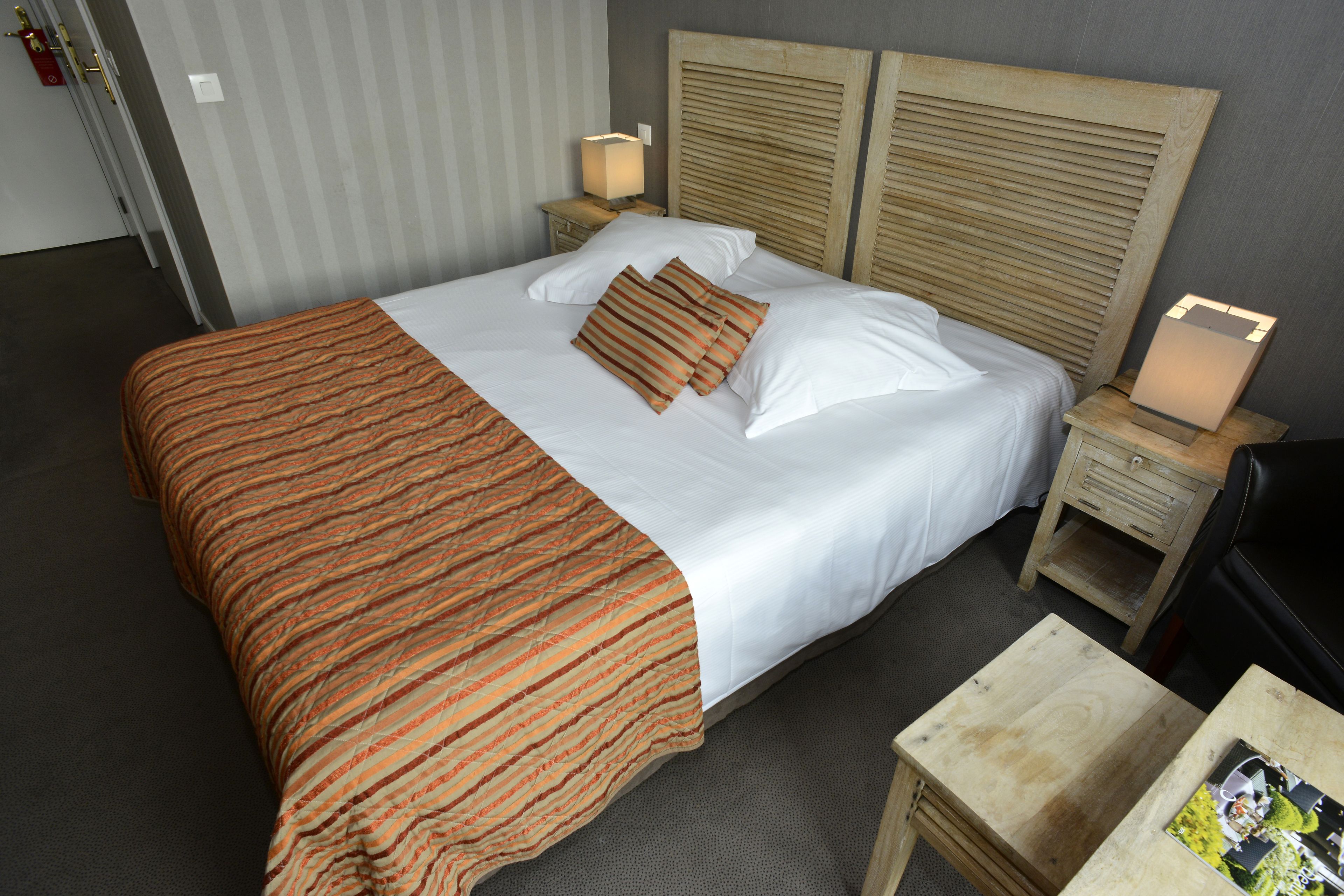 A neatly made bed with a striped blanket, two bedside tables with lamps, and a small wooden table with a magazine.