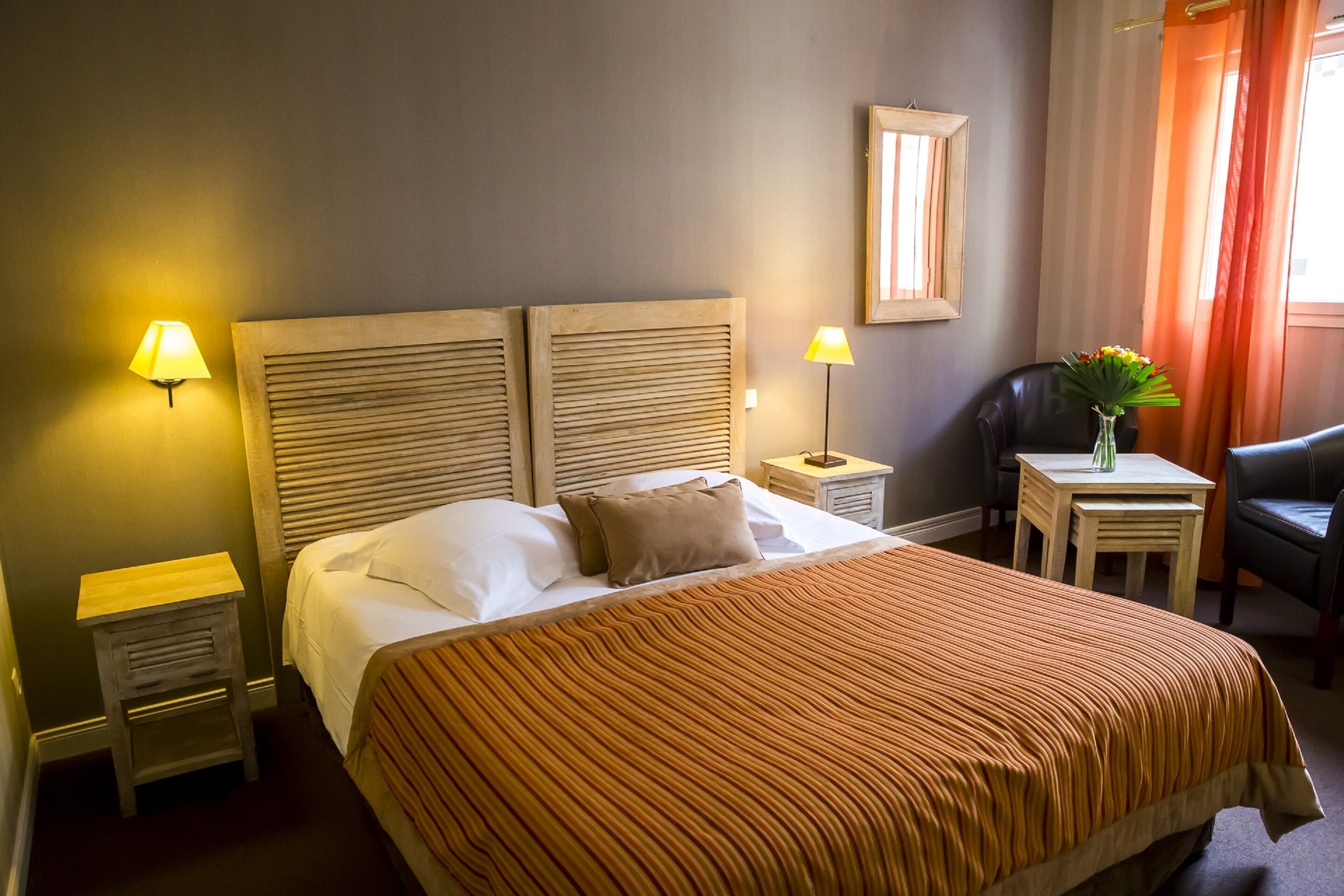 A hotel room with a large bed, two bedside tables, a chair, a small table with a vase, and a mirror on the wall.