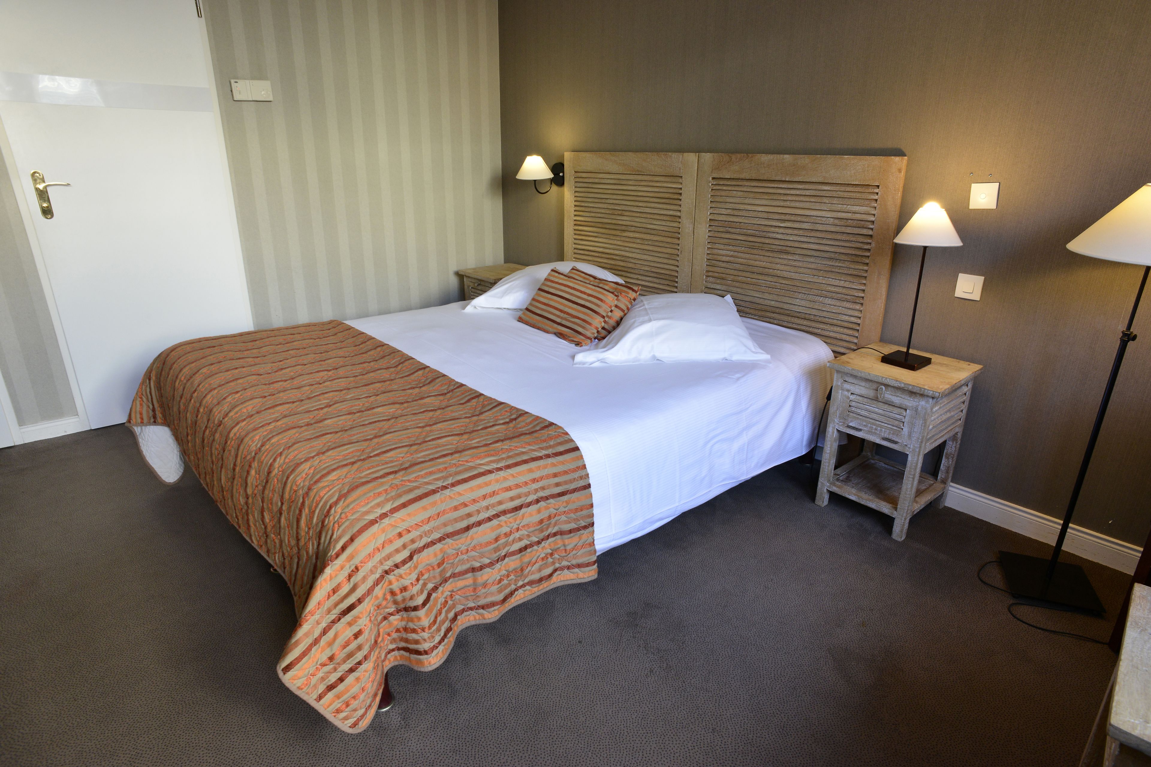A hotel room with a large bed, a wooden headboard, two bedside tables with lamps, and a door.