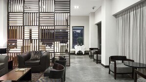 Una sala moderna con un sofá modular, sillones, una mesa de centro y un tapete estampado. Hay un comedor con mesa y sillas, y una pared decorativa con listones verticales.