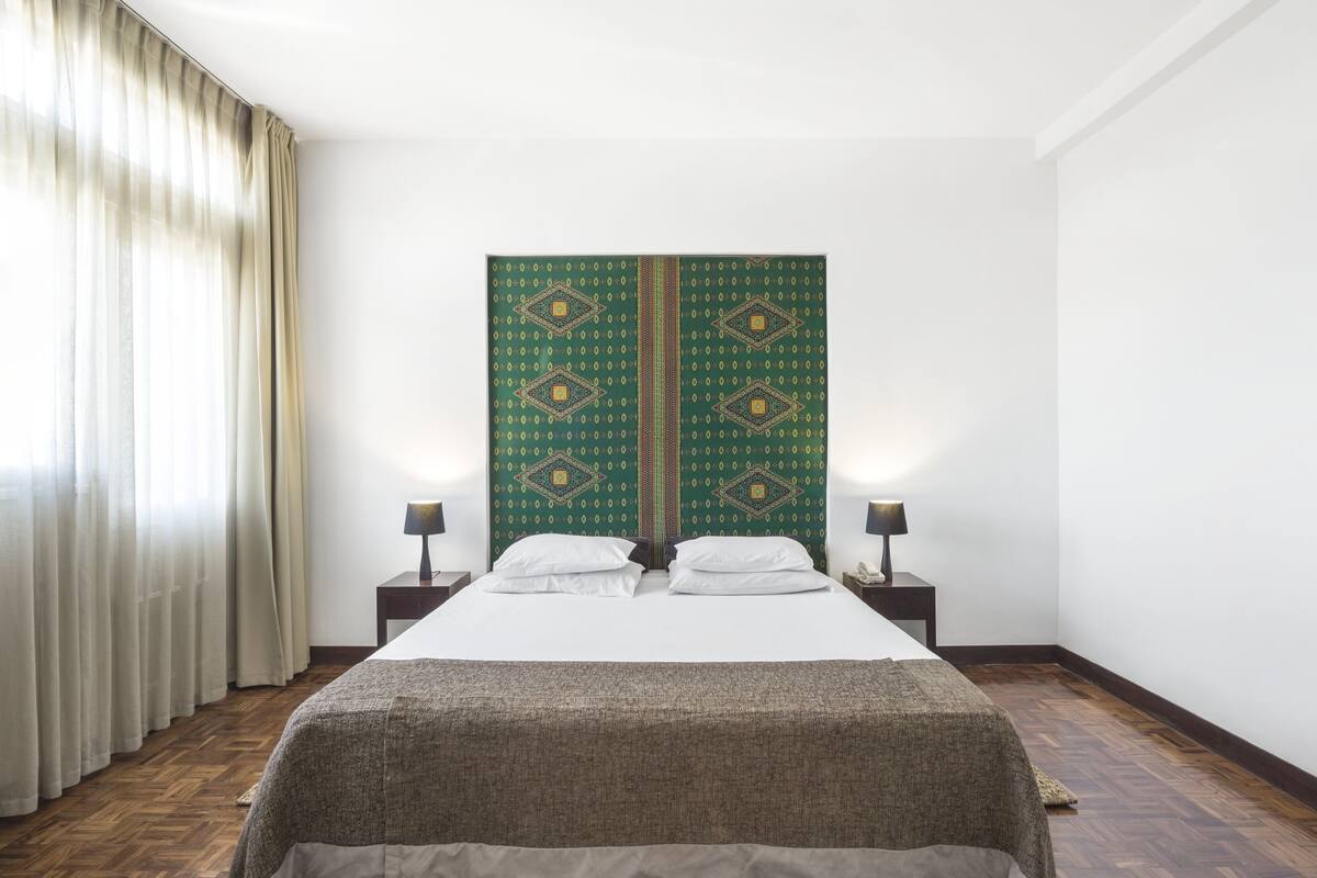 Une chambre à coucher bien aménagée, avec un grand lit, deux tables de chevet dotées de lampes et un paravent décoratif.