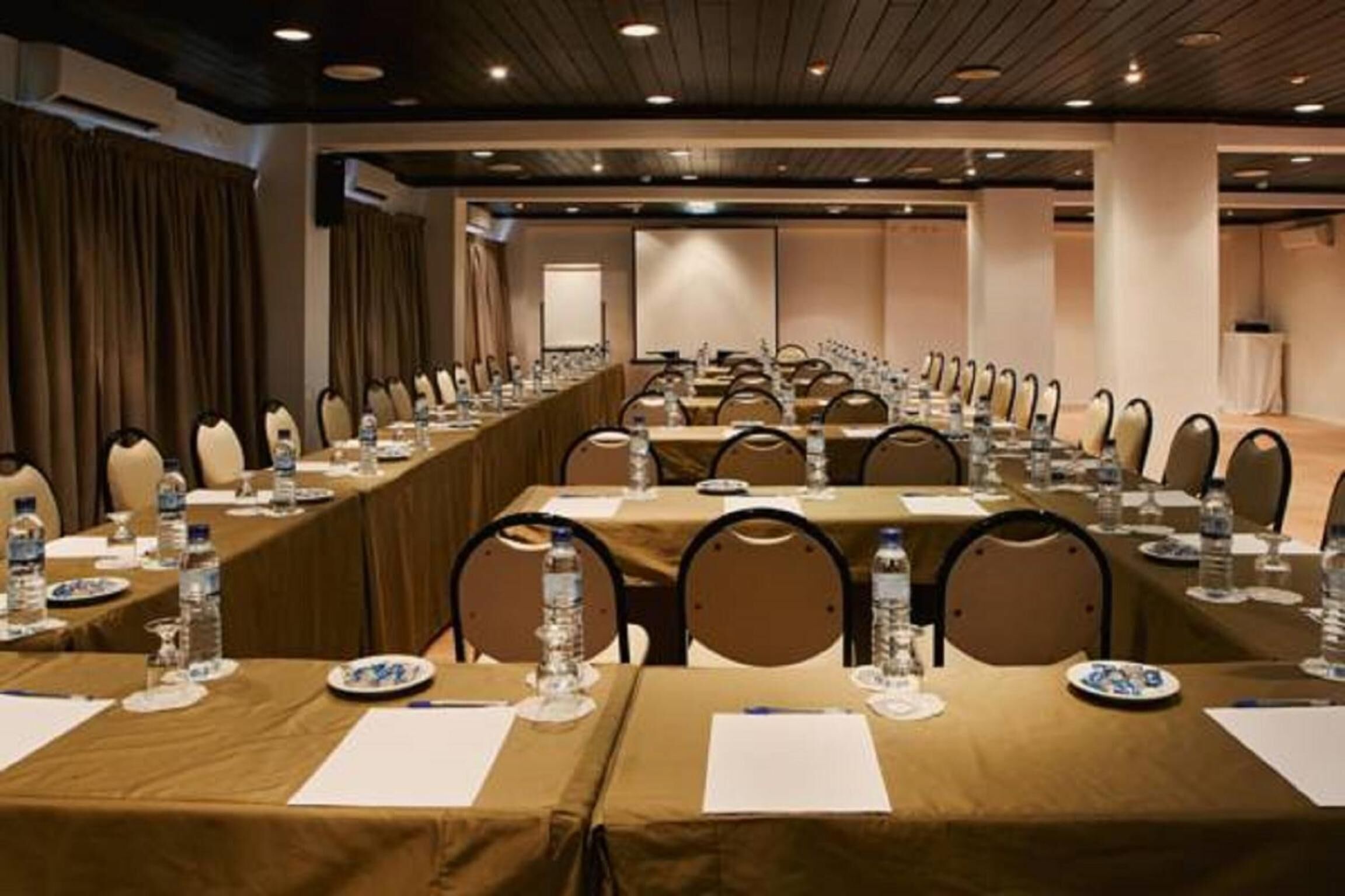 Una sala conferenze con lunghe tavolate, sedie, bottiglie d'acqua e cartellini con i nomi.