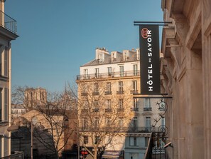 Un cartel de hotel con la inscripción "HOTEL DU SAVOIR", que indica un hotel llamado "HOTEL DU SAVOIR" en un paisaje urbano con arquitectura clásica.