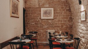 Een gezellig restaurant met stenen muren, ronde tafels en rode fauteuils.