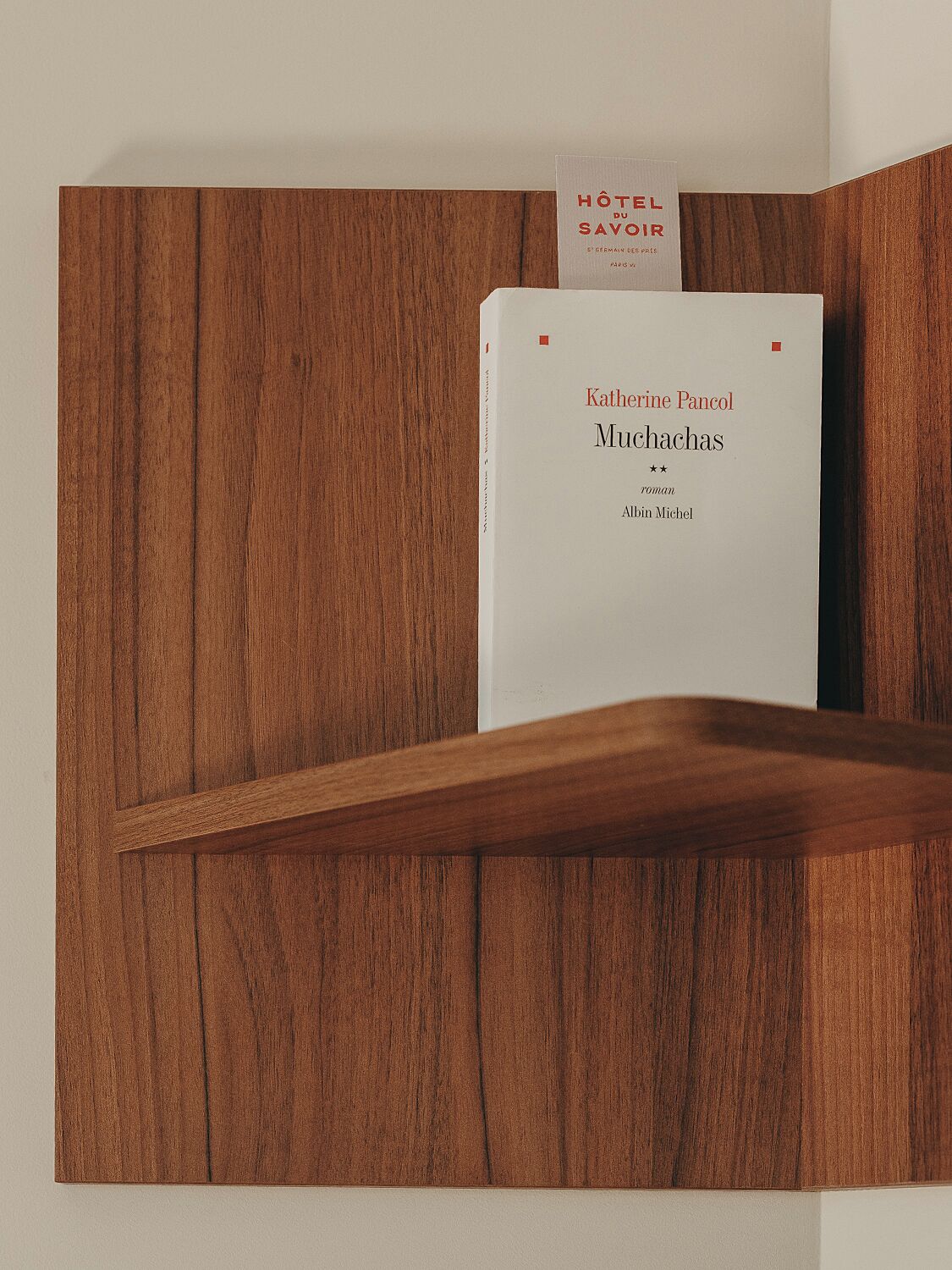 Ein Buch mit dem Titel „Muchachas“ von Katheline Pancol, platziert auf einer Holzregal an einer Wand.