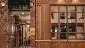 Een hotelentree met een geruite vloer, een groene deur en een bord met de tekst 'HOTEL DU SAVOIR'.
