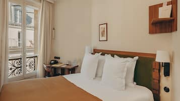 Ein Hotelzimmer mit einem großen Bett, einem Nachttisch, einer Lampe, einem Bilderrahmen an der Wand und einem Fenster mit Vorhängen.