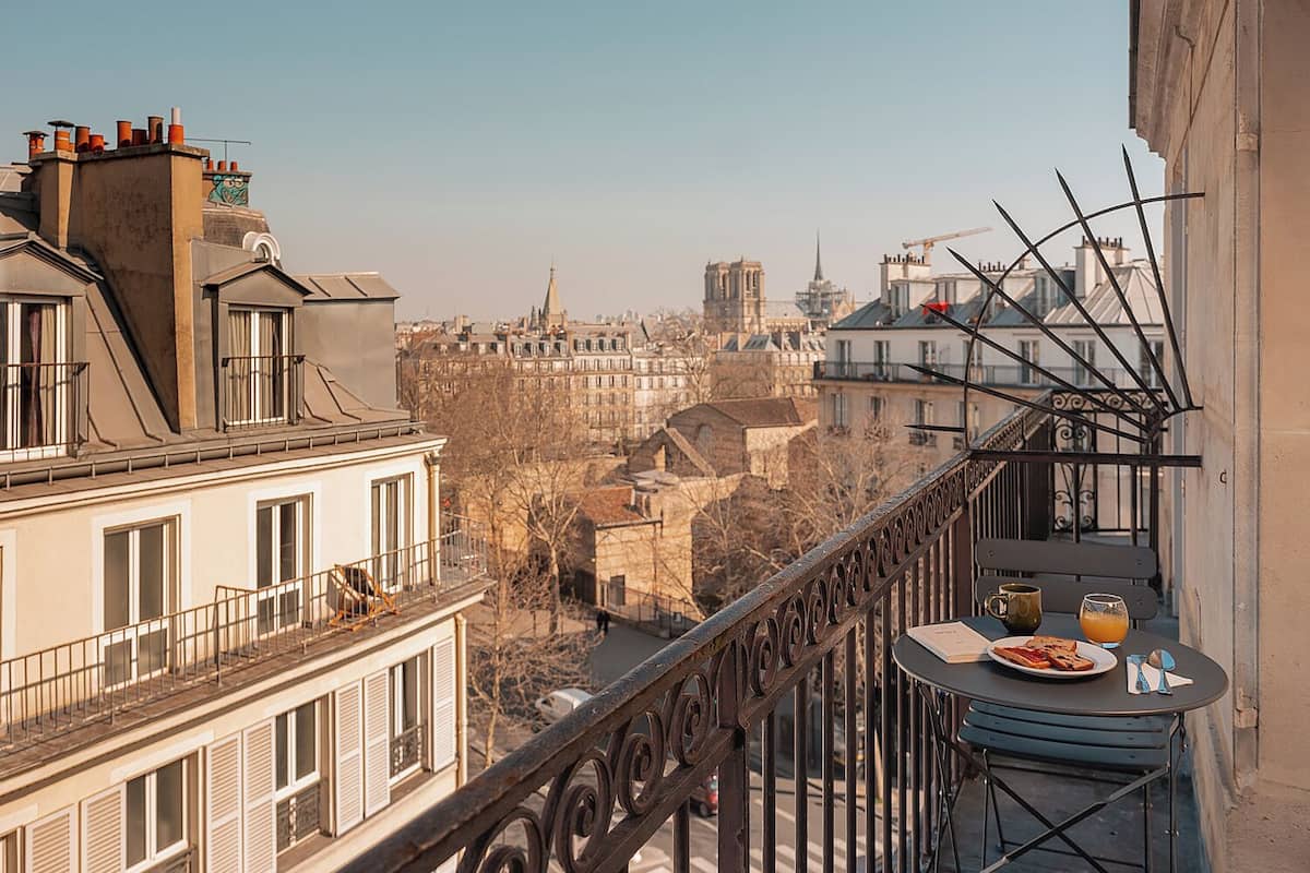 A balcony with a table set for breakfast, overlooking a cityscape with historic buildings and a church spire.