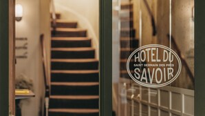 Une enseigne d’hôtel portant le nom « HÔTEL DU SAVOIR » et un escalier en arrière-plan.
