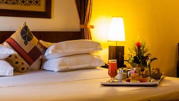 A hotel room with a neatly made bed, a tray with breakfast items, a bedside lamp, and a decorative wall piece.