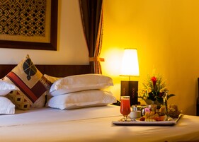 A hotel room with a neatly made bed, a tray with breakfast items, a bedside lamp, and a decorative wall piece.