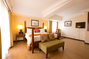 A hotel room with a four-poster bed, a bench, two bedside tables, a flat-screen TV, and artwork on the walls.