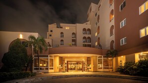A hotel entrance with a curved facade, multiple balconies, and a well-lit entrance area.