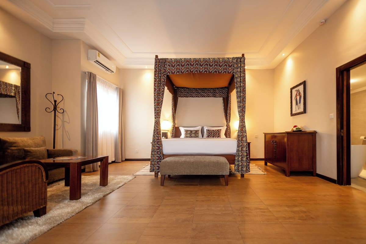 A four-poster bed with a canopy, a wooden bench, a sofa, and a small table in a hotel room.
