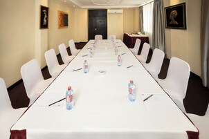 A conference room with a long table, white chairs, water bottles, and a small table with a cloth.