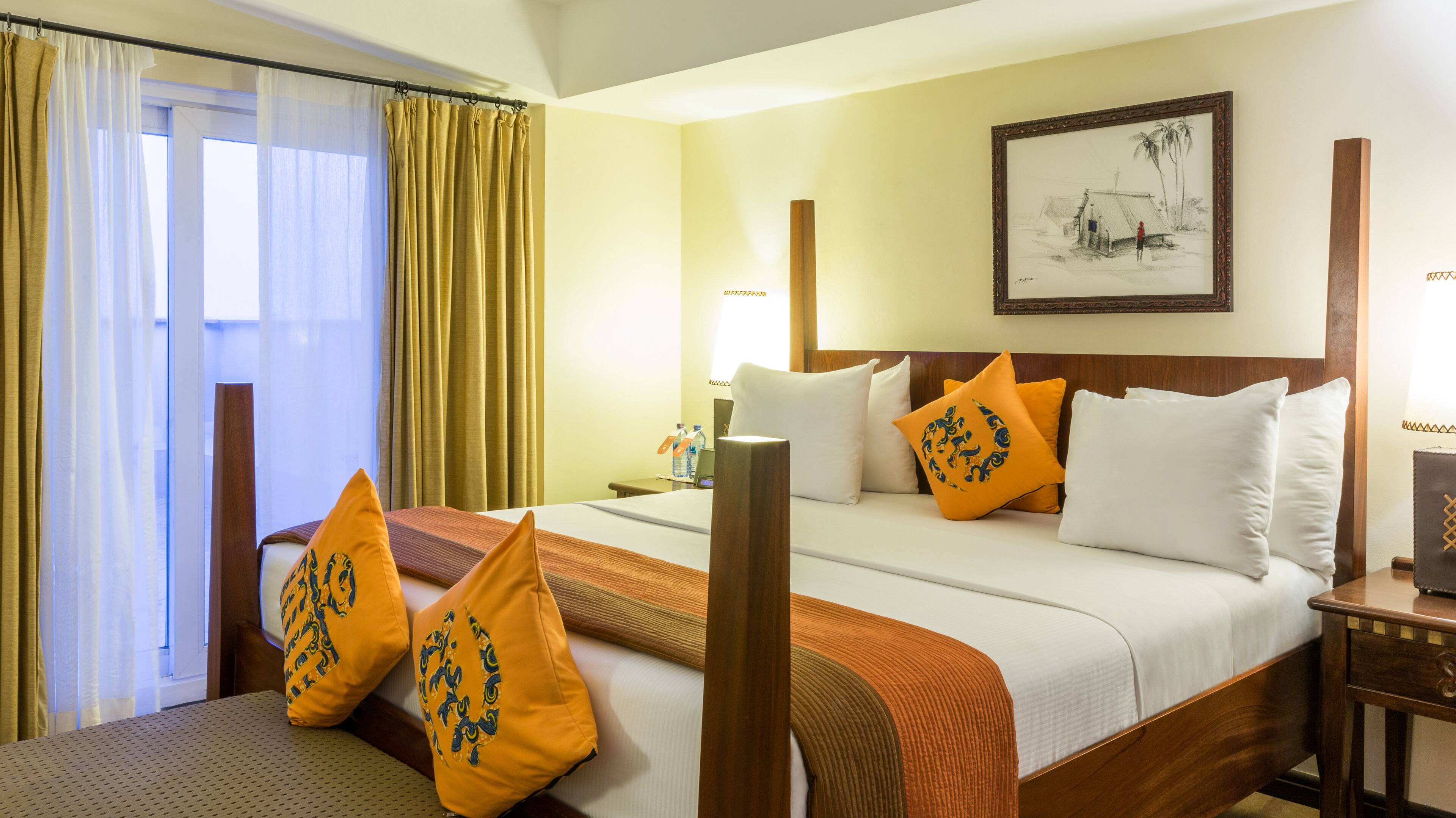 A hotel room with a bed, a nightstand, a lamp, a painting on the wall, and a window with curtains.