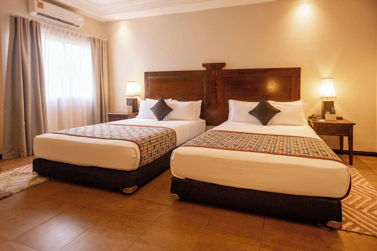 A hotel room with two beds, each with a patterned bedspread, a wooden headboard, and a nightstand with a lamp.