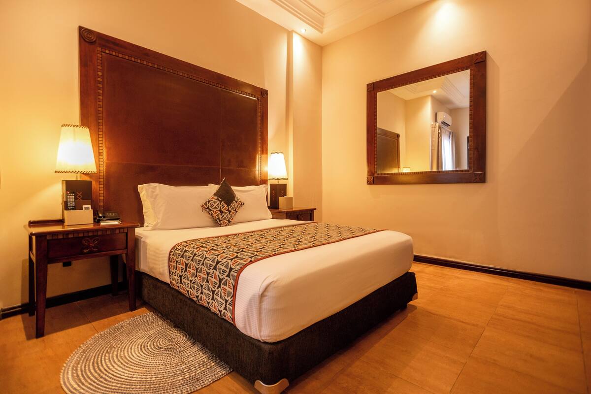 A hotel room with a large bed, two bedside tables with lamps, a round rug, and a mirror on the wall.