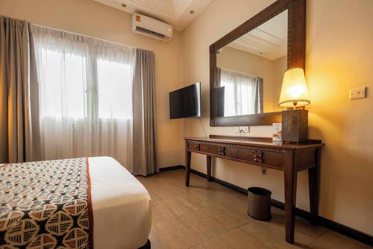 A hotel room with a bed, a TV, a desk with a lamp, and a large mirror.