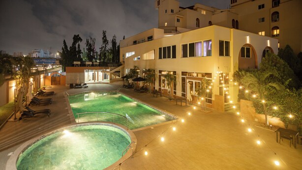 A hotel with a swimming pool, outdoor seating, and a well-lit entrance.