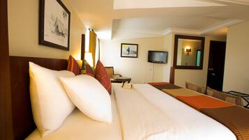 A hotel room with a large bed, a desk, a chair, a television, and a mirror.
