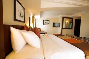 A hotel room with a large bed, a desk, a chair, a television, and a mirror.