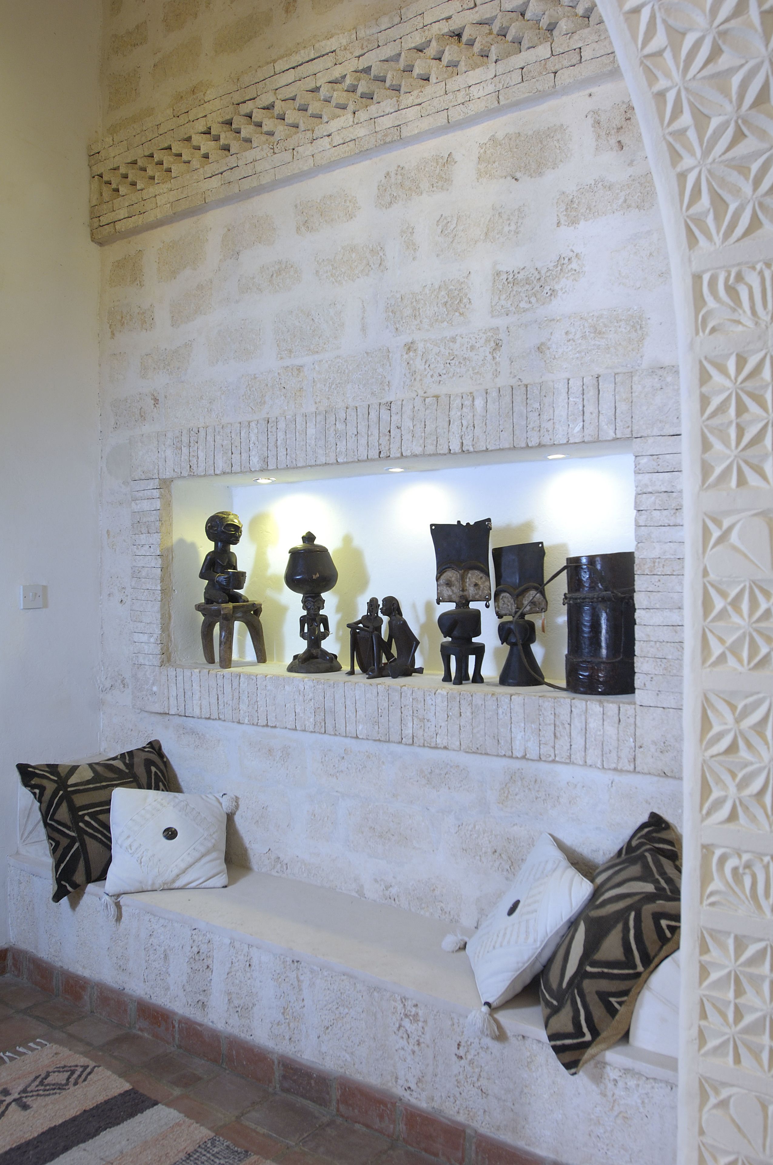A stone bench with cushions and a wall-mounted display of sculptures.
