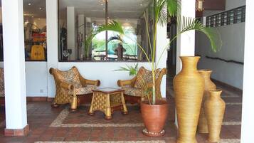 Un hall con muebles de mimbre, una planta grande en maceta y altos jarrones.