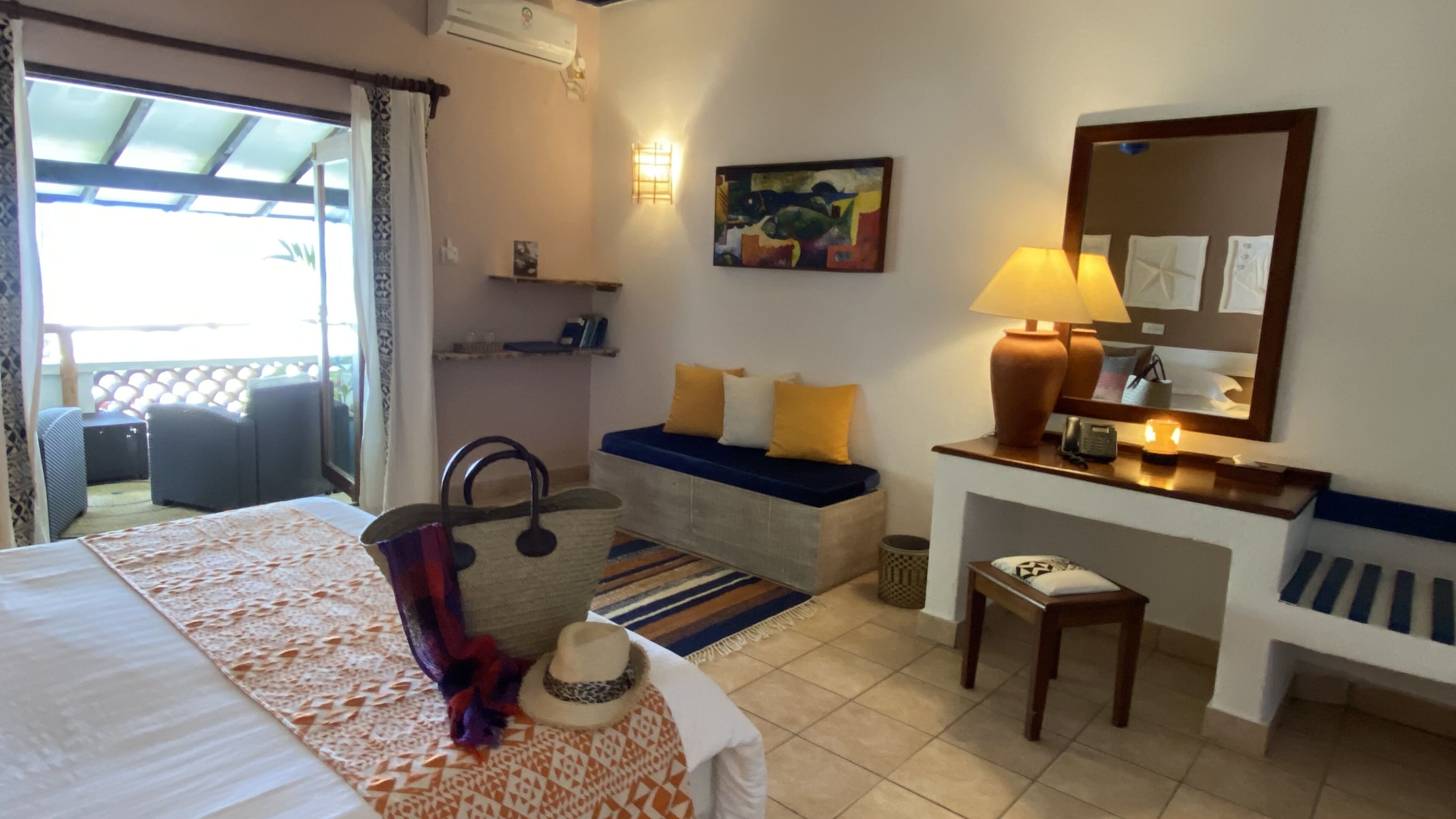 Une chambre d’hôtel comprenant un lit, un canapé, un bureau avec une lampe, une chaise, une petite table, un miroir fixé au mur et un tableau.