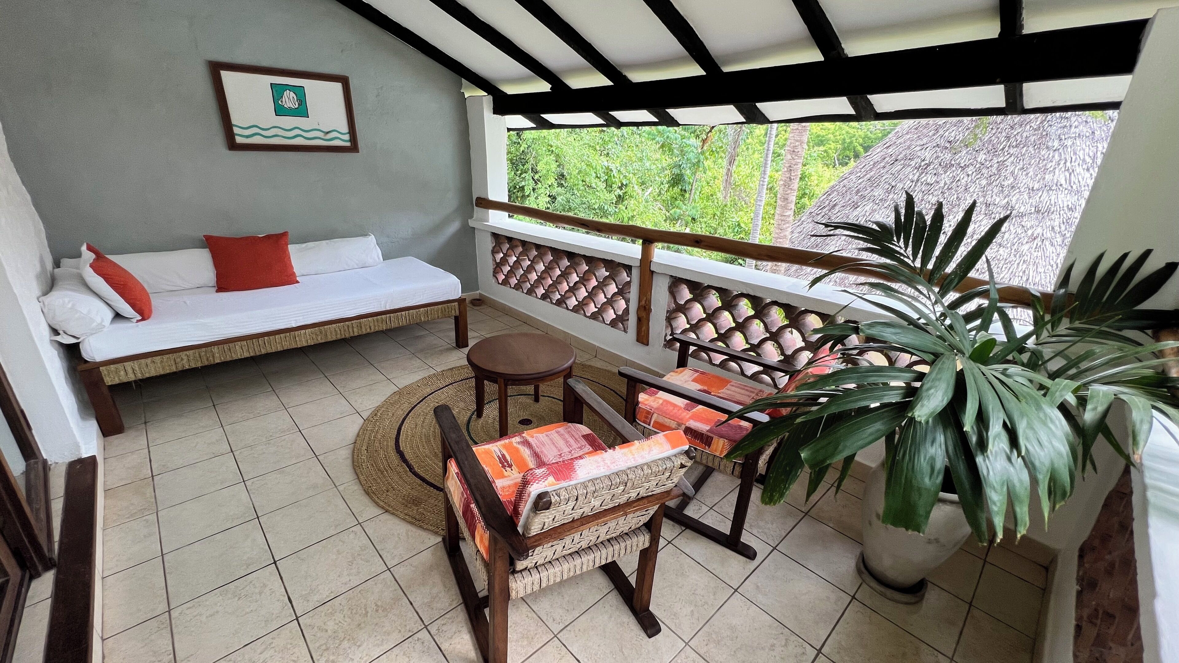 A balcony with a sofa, chairs, a table, and a potted plant.