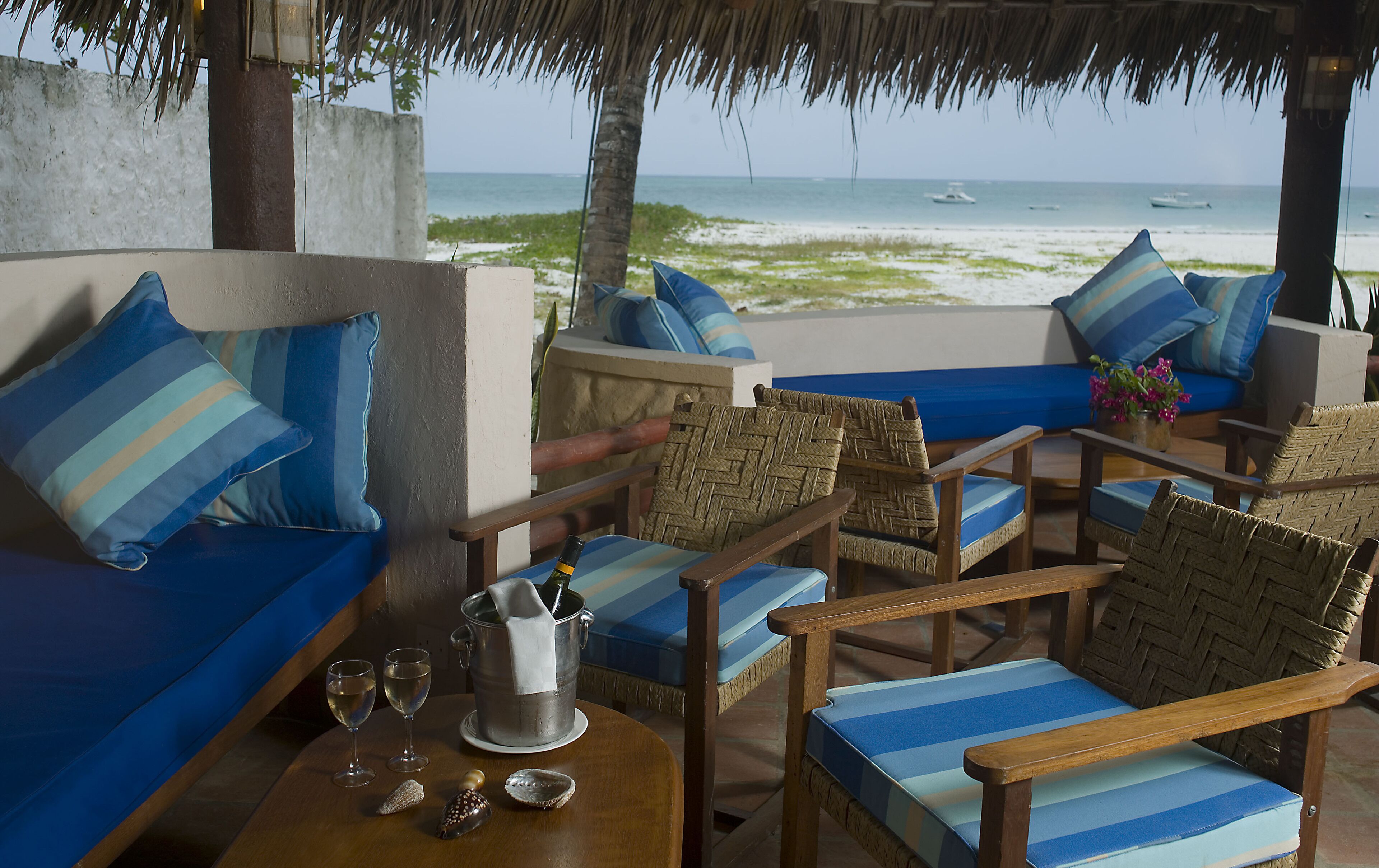 A beachside seating area with a view of the ocean, featuring striped cushions and wicker furniture.