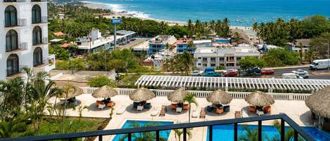 A resort with a pool, beach view, and thatched umbrellas.