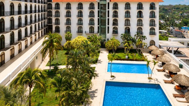Un hotel con varios balcones, piscina y jardines tropicales.