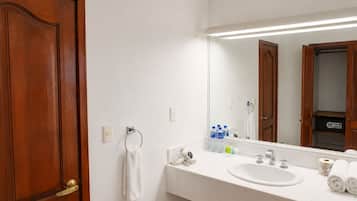 Un baño con puerta de madera, un lavabo blanco, un espejo y artículos de aseo en la encimera.