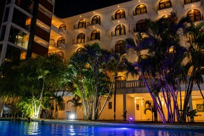A hotel with multiple balconies, a swimming pool, and tropical vegetation.
