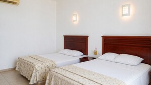 Habitación de hotel con dos camas individuales, una mesita de noche, aire acondicionado de pared y dos apliques.