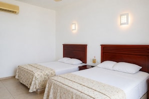 Habitación de hotel con dos camas individuales, una mesita de noche, aire acondicionado de pared y dos apliques.