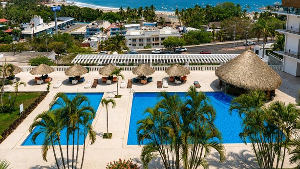 Un resort con una piscina grande, sillones de descanso y vista a la playa y al océano.