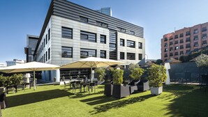 A modern building with a flat roof and large windows. There is a patio area with outdoor furniture and umbrellas. - Hotel Nuevo Boston (Madrid)