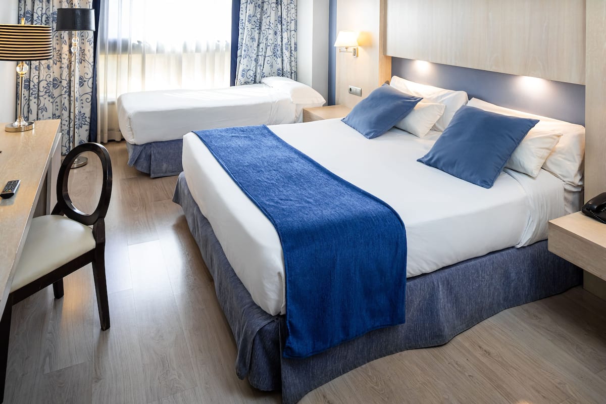 A hotel room with two beds, a desk, a chair, and a lamp.