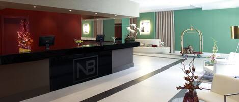 Un moderno vestíbulo de hotel con mostrador de recepción, zona de estar y plantas decorativas.