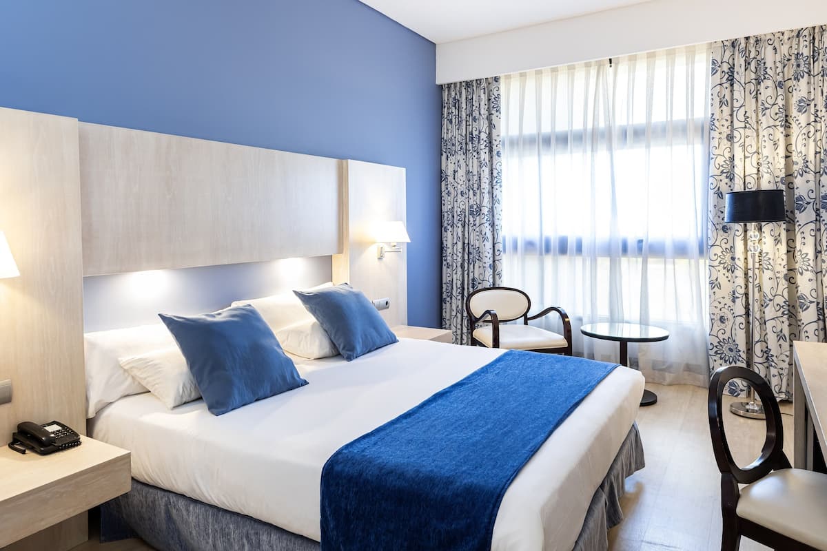 A hotel room with a large bed, bedside tables, a desk, and a chair.