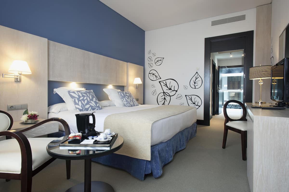 A hotel room with a bed, bedside tables, a desk, and a chair.
